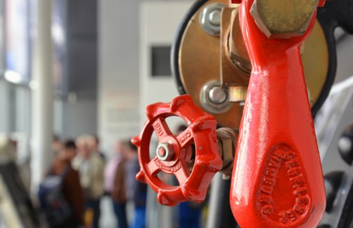 Die Detailaufnahme des Kessels, der in der Technikhalle steht, zeigt einen Hebel und ein kleines Rad. Beide sind rot und heben sich sehr schön vom sonst schwarzen Kessel ab.