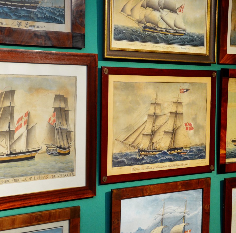 Es hängen viele verschiedenen Schiffportraits im Flensburger Schifffahrtsmuseum. Sie hängen dicht an dicht auf einer grünen Wand. Sie zeigen unterschiedliche in Flensburg gebaute Schiffe.