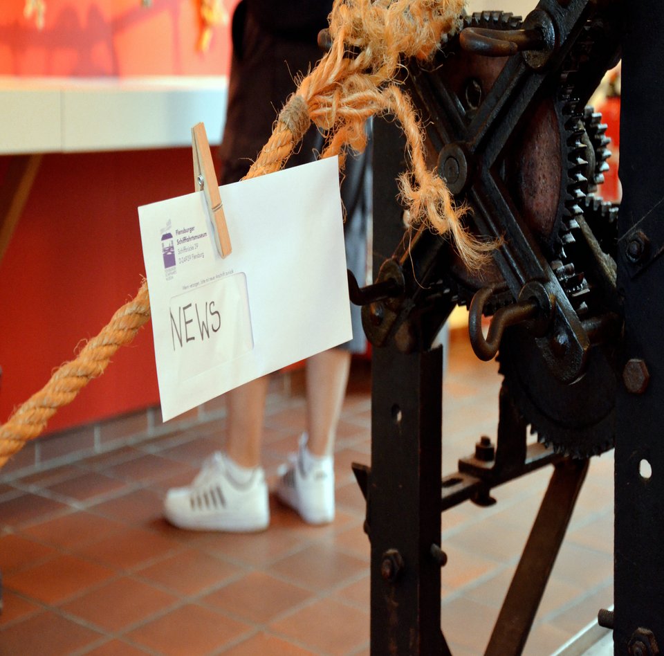 In der Ausstellung "Tauwerk und Takelage" steht eine Reepschlagmaschine. Es sieht so aus, als würde gerade ein Seil hergestellt werden. An dem Seil ist ein Briefumschlag mit der Aufschrift "News" mit einer Wäscheklammer befestigt.