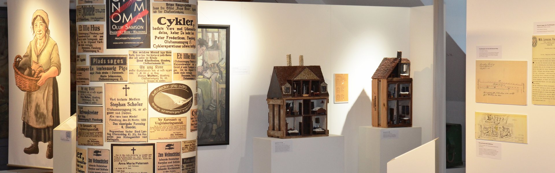 I midten af udstillingen IDYL OG KONFLIKT står en reklamestolpe, der er overklistret med forskellige gamle avisannoncer. Alle handler om Oluf-Samson-gangen. Bagved står modeller af to huse fra gangen. De står foran en skillevæg. På denne hænger et maleri, der viser en skomager. Til venstre i baggrunden ses et stort banner. Det viser en middelaldrende kvinde, der bærer en kurv med keramik i hånden. Hendes tøj er enkelt og lidt snavset.