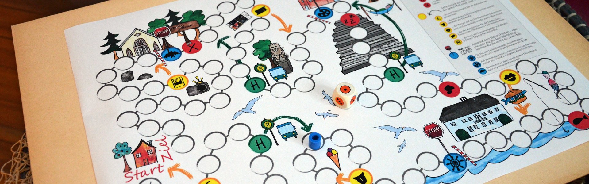 Ein Brettspiel liegt auf einem Fischernetz, das wiederum über einem Fass hängt. Auf dem Spielbrett sind zwei Figuren und ein Würfel platziert. Das Spielfeld besteht aus mehreren kreisrunden Feldern. Zudem sind verschiedene Zeichnungen rund um das Spielfeld gemalt.