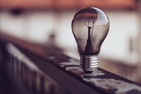 Auf dem Foto ist eine Glühlampe zu sehen. Sie brennt nicht. Sie steht auf einem Geländer. Der Hintergrund ist verschwommen.