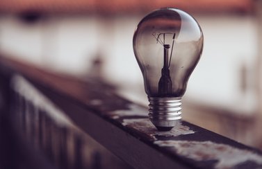 Auf dem Foto ist eine Glühlampe zu sehen. Sie brennt nicht. Sie steht auf einem Geländer. Der Hintergrund ist verschwommen.