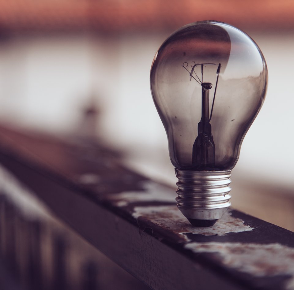 Auf dem Foto ist eine Glühlampe zu sehen. Sie brennt nicht. Sie steht auf einem Geländer. Der Hintergrund ist verschwommen.