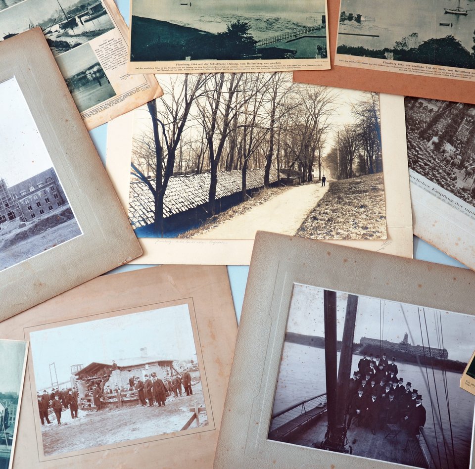 På et bord ligger der forskellige gamle fotos og avisartikler med billeder. Nogle af fotografierne har passepartout. Men ingen af dem er indrammet.