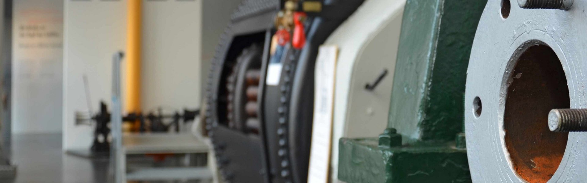 Man sieht die Technik-Halle. An den Wänden stehen Maschinen. Hinten ist die Brücke von einem Schiff angedeutet.