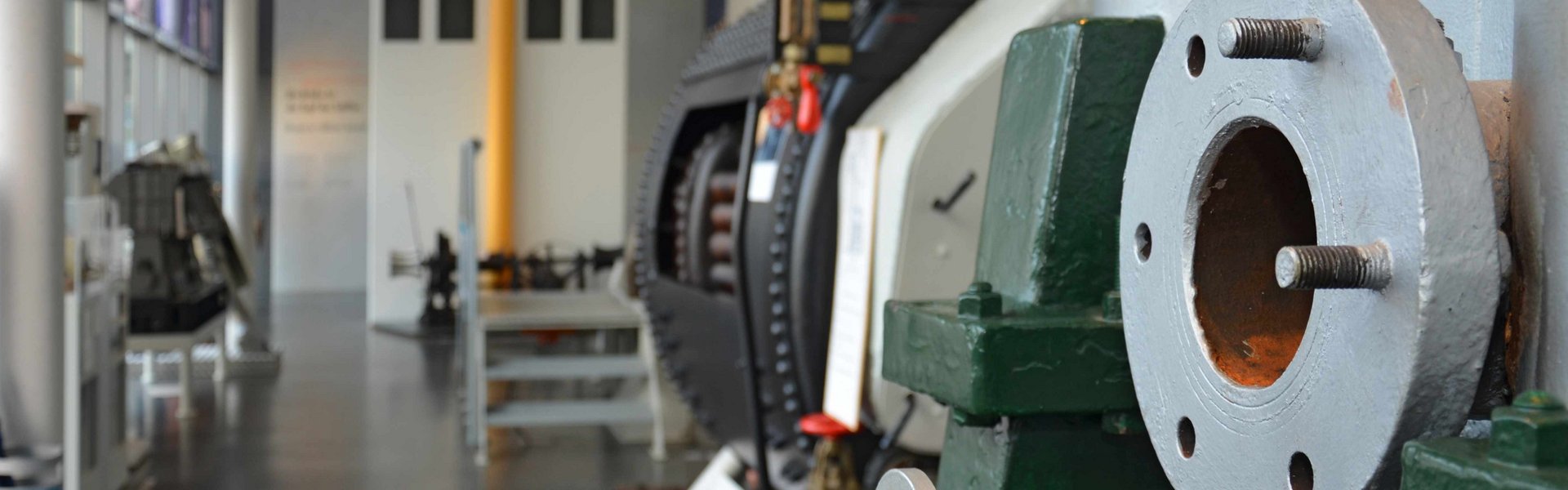 Blick durch die Technikhalle. Rechts und links an den Wänden stehen verschiedene Maschinen. Auch im Vordergrund ist eine große Maschine zu erkennen. Im Hintergrund ist die Brücke eines Schiffes angedeutet.