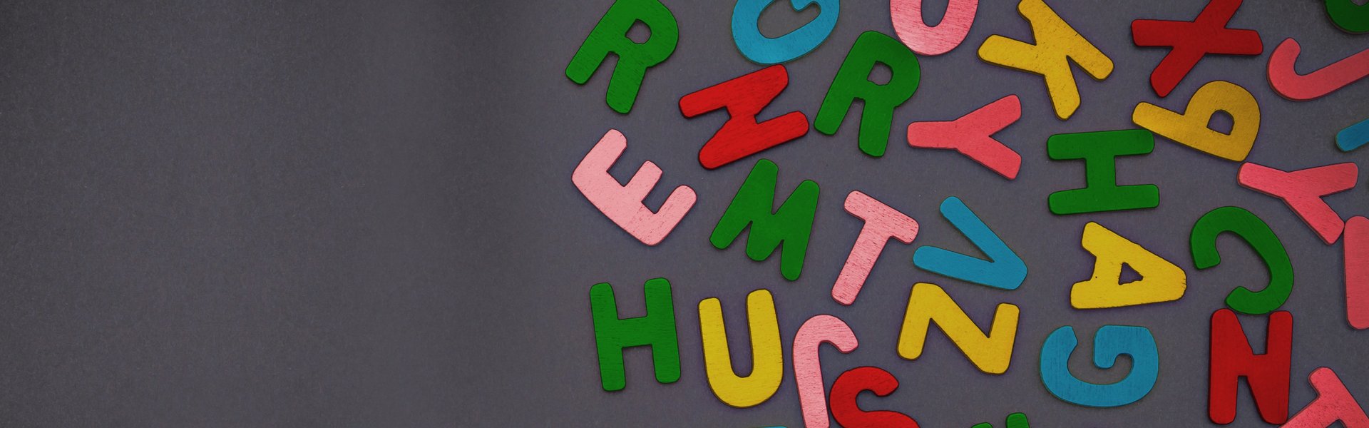 Farbige Holzbuchstaben liegen auf einem schwarzen Grund.