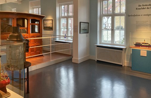 Die Ausstellung FÖRDESCHIFFFAHRT besteht aus einem Steuerhaus und verschiedenen Schiffsmodellen und Schiffsportraits.