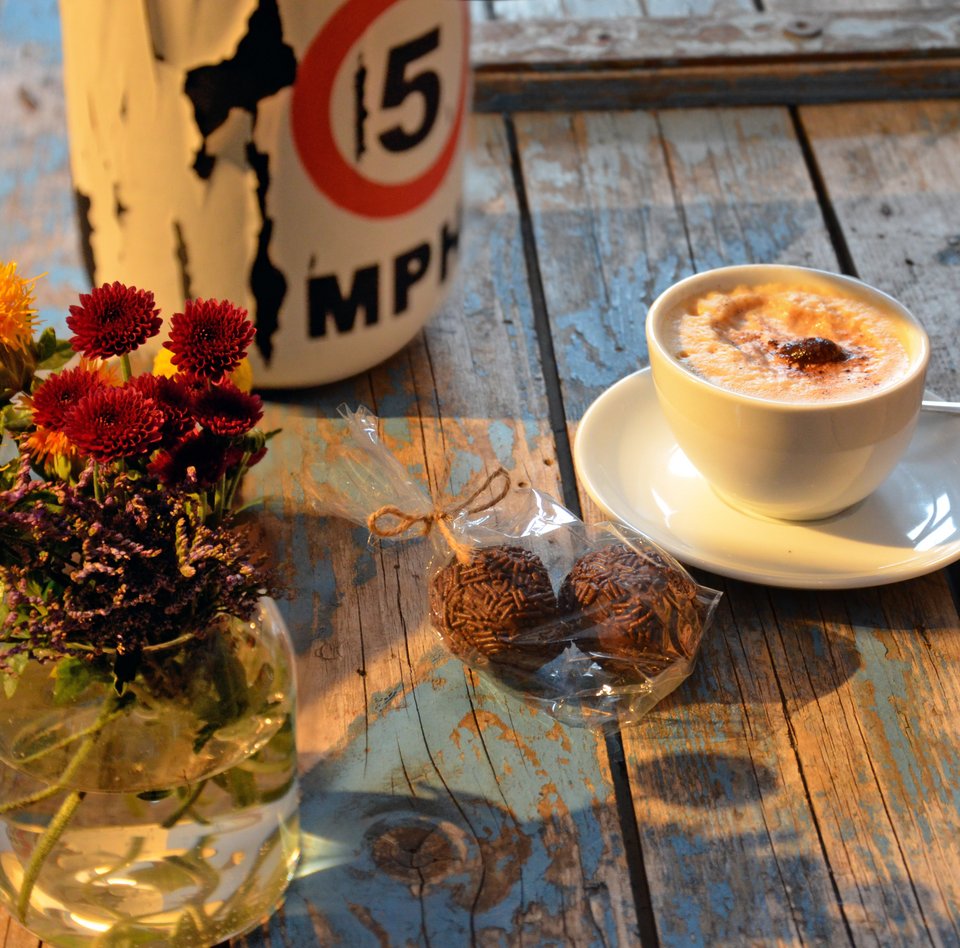 Auf einer alten Kiste steht eine Blumenvase, daneben eine Lampe. Auch eine Tasse Cappuccino und zwei Rumkugeln in einer Tüte sind auf der Kiste, die im Café des Schifffahrtsmuseums als eine Art Tresen dient. 