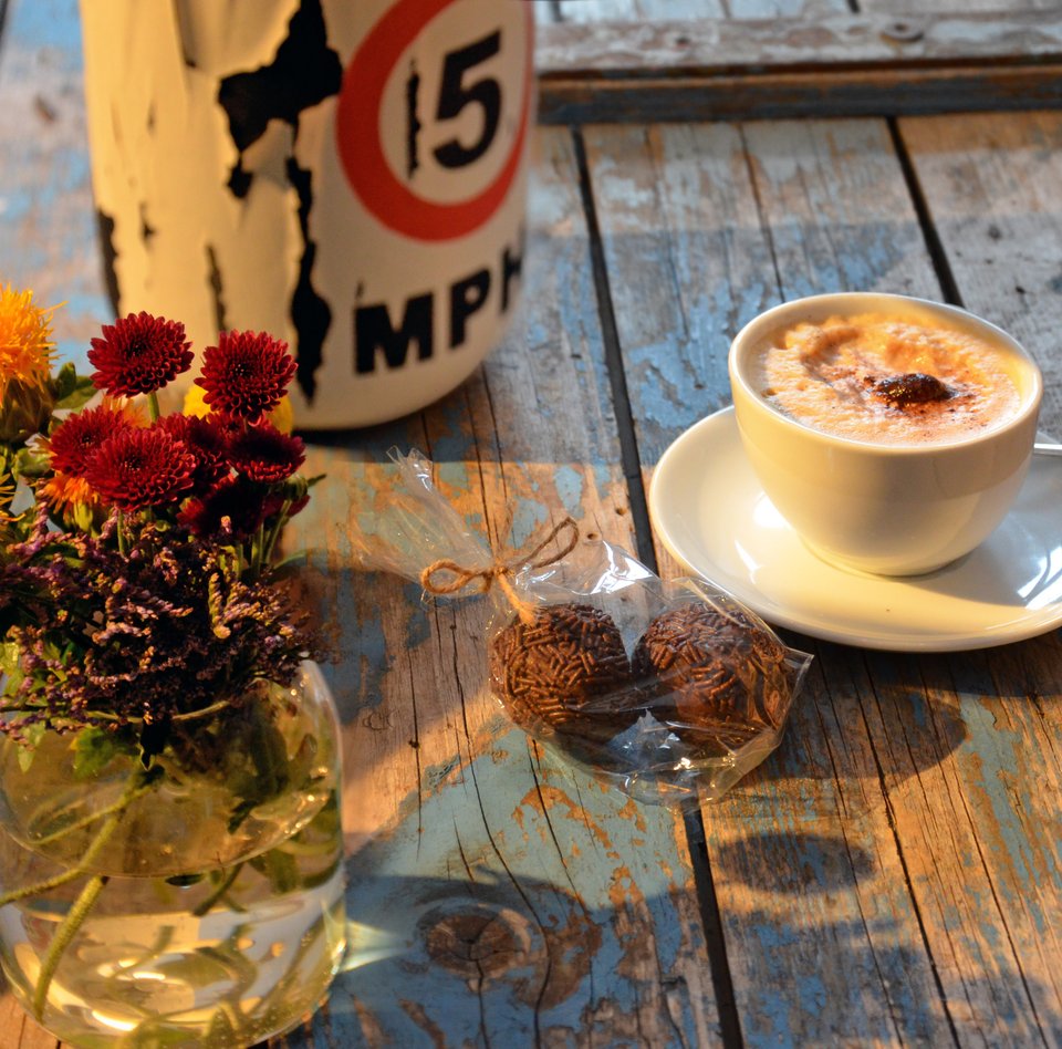 Auf einer alten Kiste steht eine Blumenvase, daneben eine Lampe. Auch eine Tasse Cappuccino und zwei Rumkugeln in einer Tüte sind auf der Kiste, die im Café des Schifffahrtsmuseums als eine Art Tresen dient. 