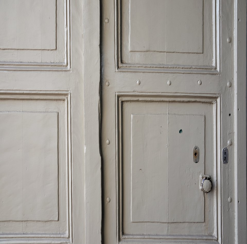 Das Schifffahrtsmuseum hat zwei große Tore. Das eine von ihnen ist hier auf dem Foto in einer Detailansicht festgehalten. Es dient als Eingang. Das Tor steht offen und ist beige bemalt. Es hat einen Knauf. 