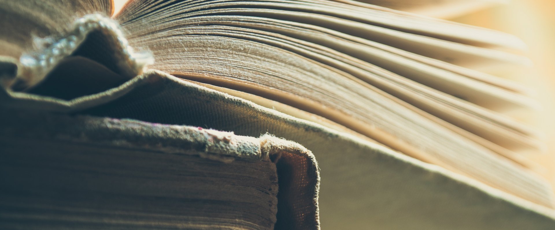 Das Foto ist eine Detailaufnahme von zwei Büchern. Ein Buch liegt auf einem anderen. Das obere ist aufgeschlagen.