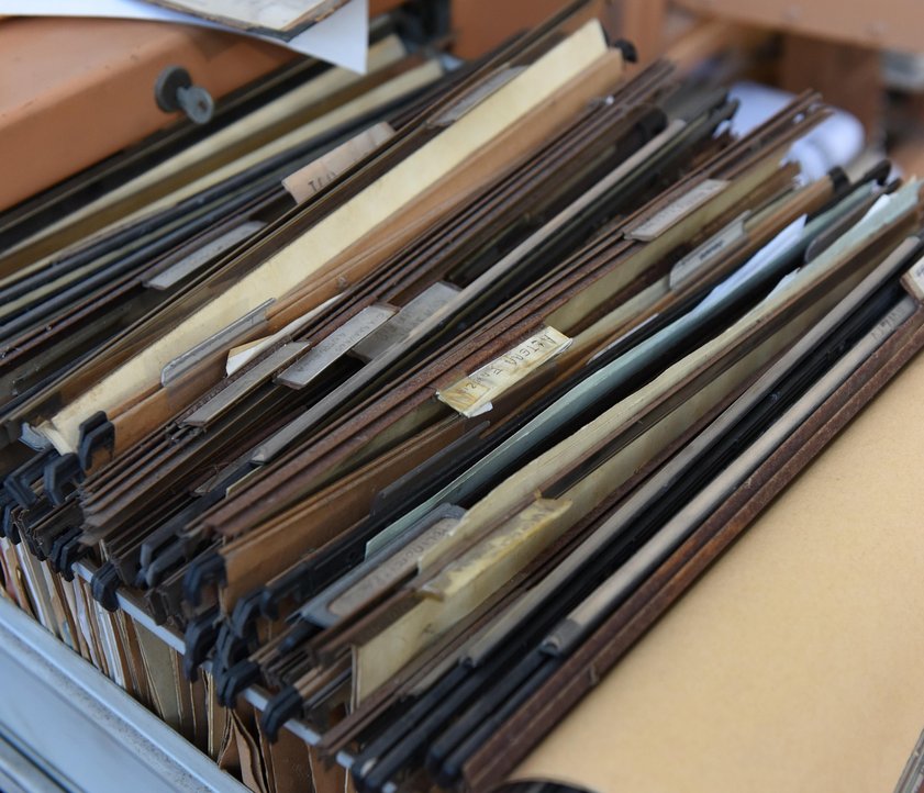 Auf dem Foto ist ein Aktenschrank zu sehen. Eine Schublade ist geöffnet. In dieser sind viele Akten einsortiert.