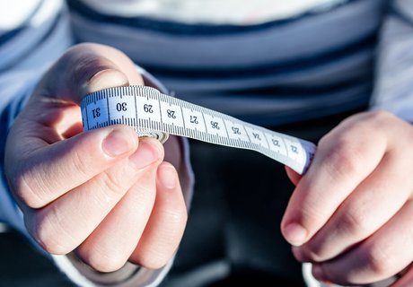 Eine Person in einem blau-weiß-gestreiften Pullover hält ein Maßband in den Händen. In der einen Hand ist das aufgerollte Ende und in der anderen Hand der Anfang.