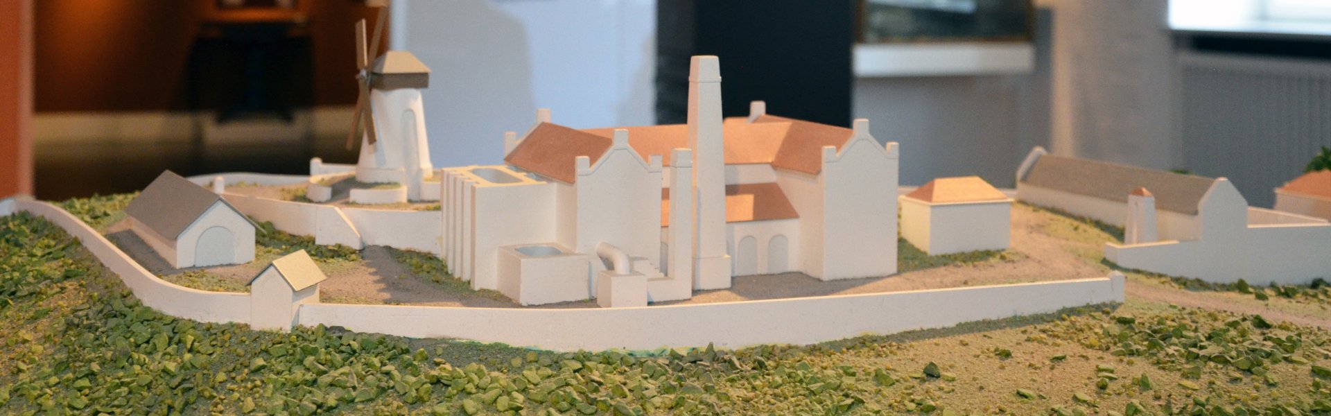 Det farvede fotografi viser en sukkerrørsplantage. Bagved ses en brun søjle med glas i midten. Bagved dette ses en træfigur, som er lagt i lænker. Bagved søjlen ses et kort, som er printet på væggen. Det viser trekantshandelen. Helt i baggrunden ses et andet rum med malerier af skibe og et portræt.