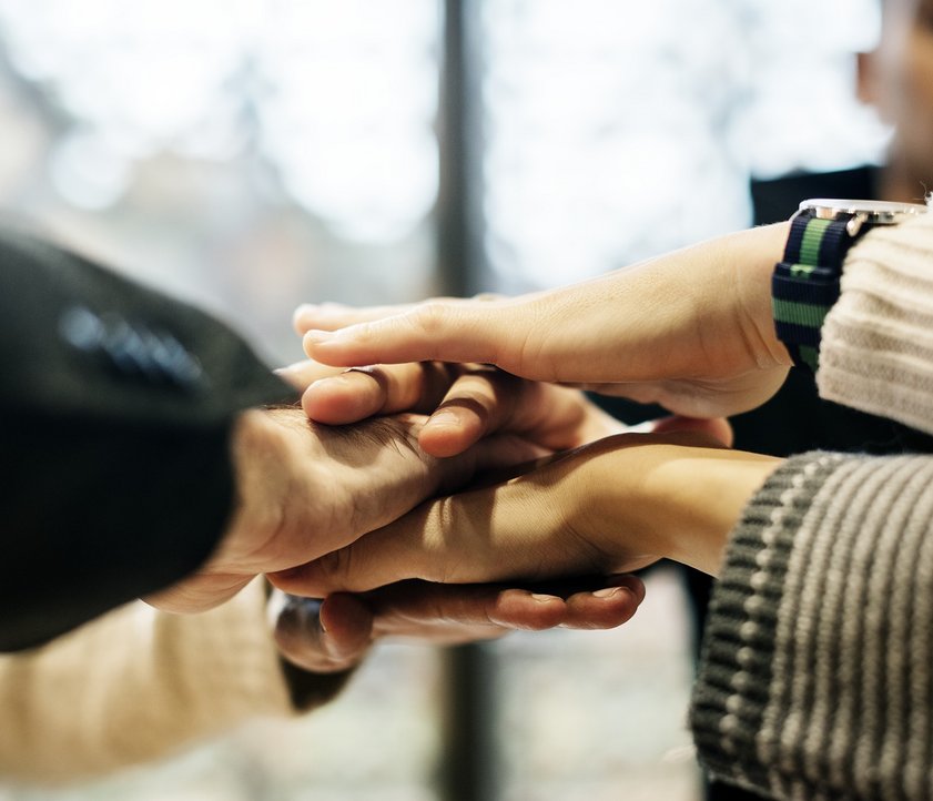 Auf dem Foto sind verschiedene Hände zu sehen, die in die Mitte gehalten werden und übereinander liegen.