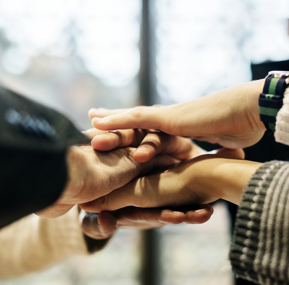 Auf dem Foto sind verschiedene Hände zu sehen, die in die Mitte gehalten werden und übereinander liegen.