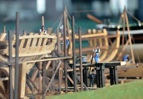 Detailaufnahme eines Modells, das zeigt, wie früher Schiffe gebaut worden sind. Im Vordergrund ist das Gerippe eines Segelschiffes aus Holz zu sehen. Im Modell sind viele kleine Figürchen platziert, die die Arbeiter auf dem Schiffbauplatz darstellen sollen. Eine hält beispielsweise einen Hammer in der Hand.