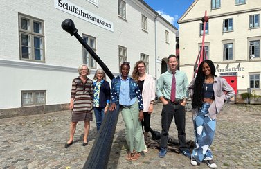 Sechs Menschen stehen an einem großen Anker vor dem Flensburger Schifffahrtsmuseum. 