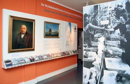 In Flensburg wurde der Rum aus der Karibik weiterverarbeitet. Rechts ist eine alte Fotografie zu sehen. Diese ist auf einer Stellwand angebracht. Auf dem Foto kann man sehen, wie vorwiegend Frauen Rumflaschen einpacken. Links an der Wand ist ein großes Portrait, das einen Mann zeigt. Hierbei handelt es sich um Heinrich Pott, der den bekannten Pott-Rum verkaufte.