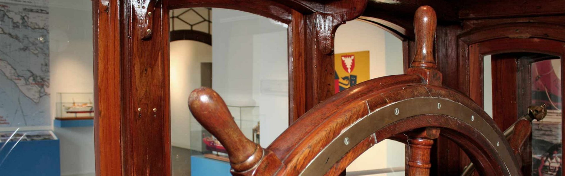 Das Foto zeigt den Blick aus dem Steuerhaus HABICHT in die Ausstellung FÖRDESCHIFFAHRT im Flensburger Schifffahrtsmuseum. Im Steuerhaus ist ein großes Ruder bzw. Steuerrad mit dem das Schiff früher gesteuert worden ist.