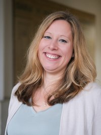 Vor einem verschwommenen Hintergrund steht eine Frau. Sie lächelt in die Kamera.