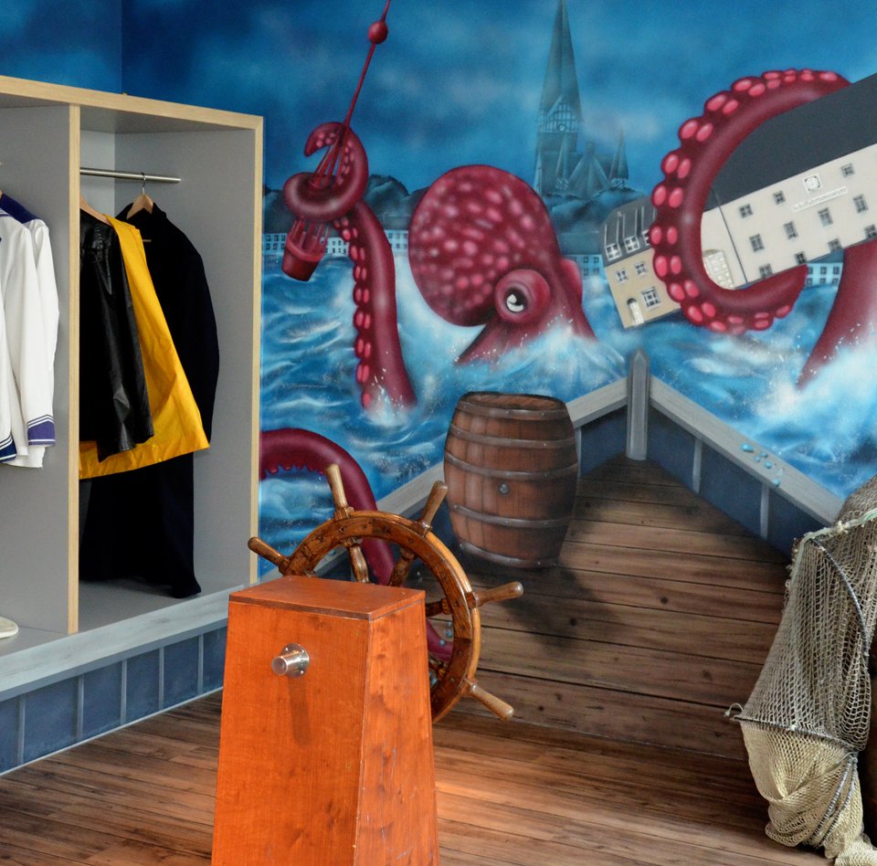 Im Flensburger Schifffahrtsmuseum kann man sich verkleiden und vor einer Wand fotografieren. Auf der Wand ist ein Bild von einem Riesenkraken gesprüht, der das Gebäude des Schifffahrtsmuseums mit seinem Tentakel festhält. Das Graffiti deutet an, dass man sich auf einem Schiff befindet und direkt auf den Riesenkraken zusteuert.