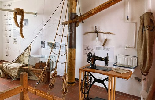 Neben einem Modell eines Mastes steht eine alte Nähmaschine mit manuellem Fußpedal.  